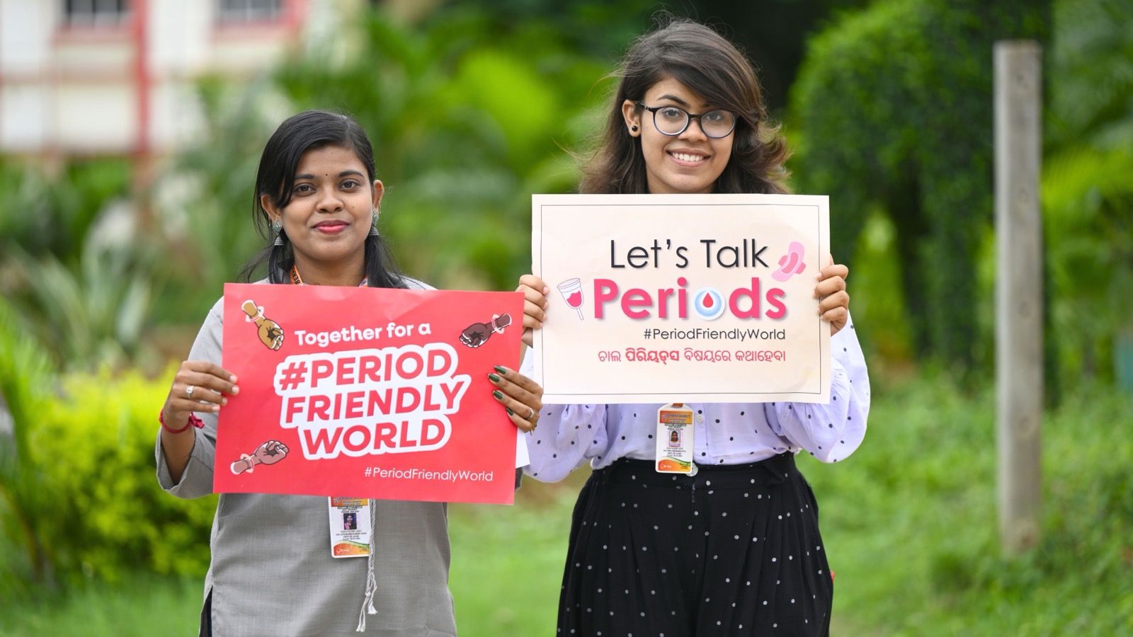 Young women holding Let's Talk Periods and Period Friendly World campaign placards